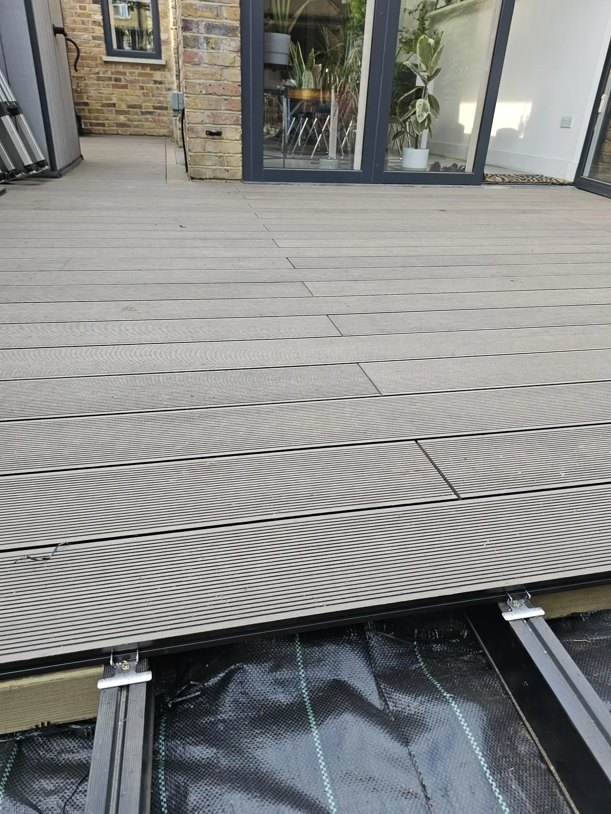 New decking boards being laid over an aluminium frame and weed membrane next to the house