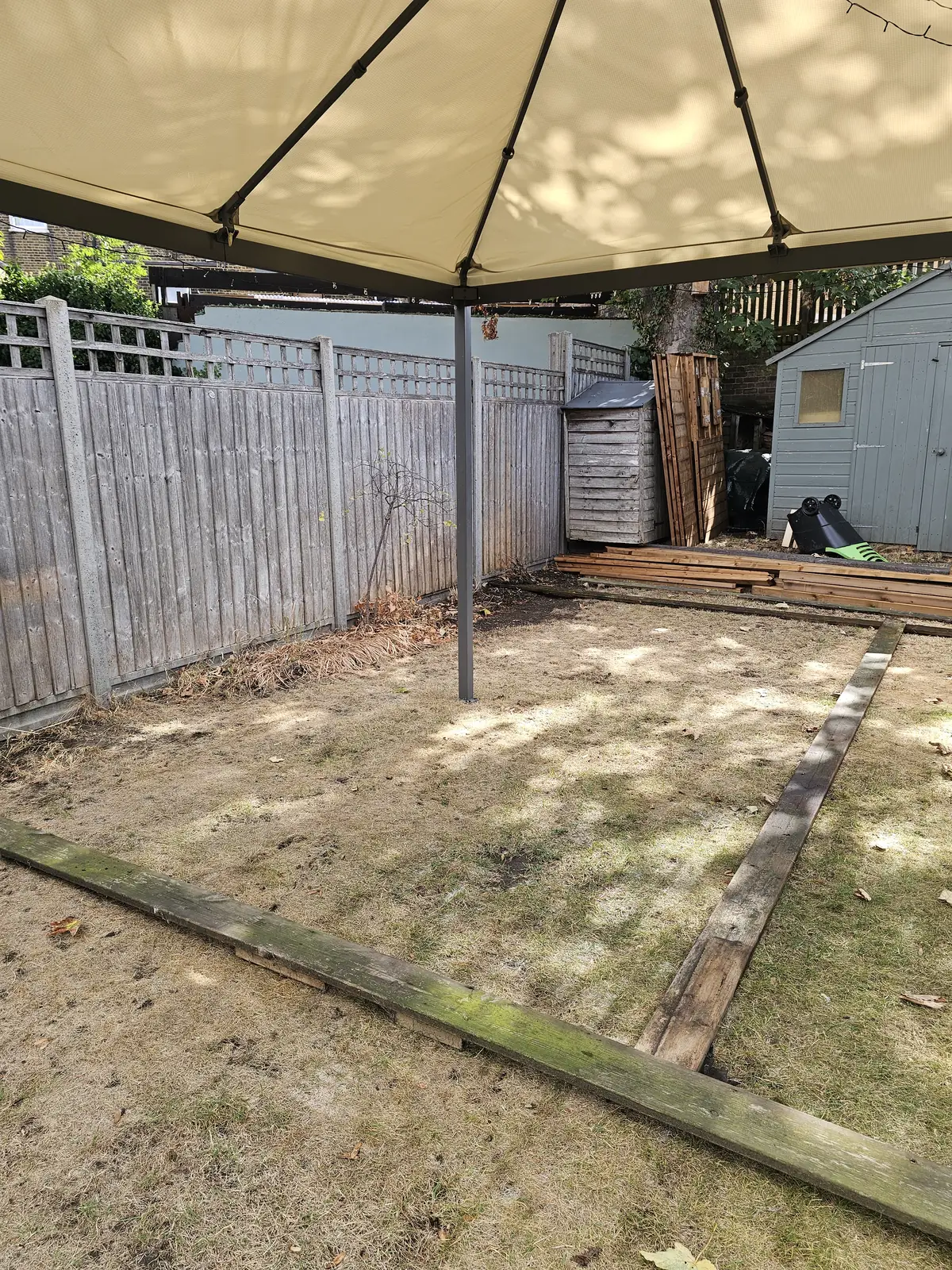 The garden before the work: bare lawn, the old fence and timber bearers on the ground