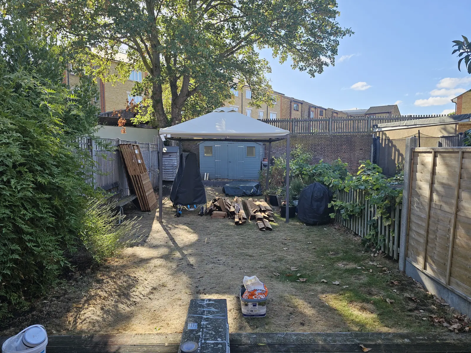 The garden before the work: dry lawn, a canvas gazebo and stacked timber