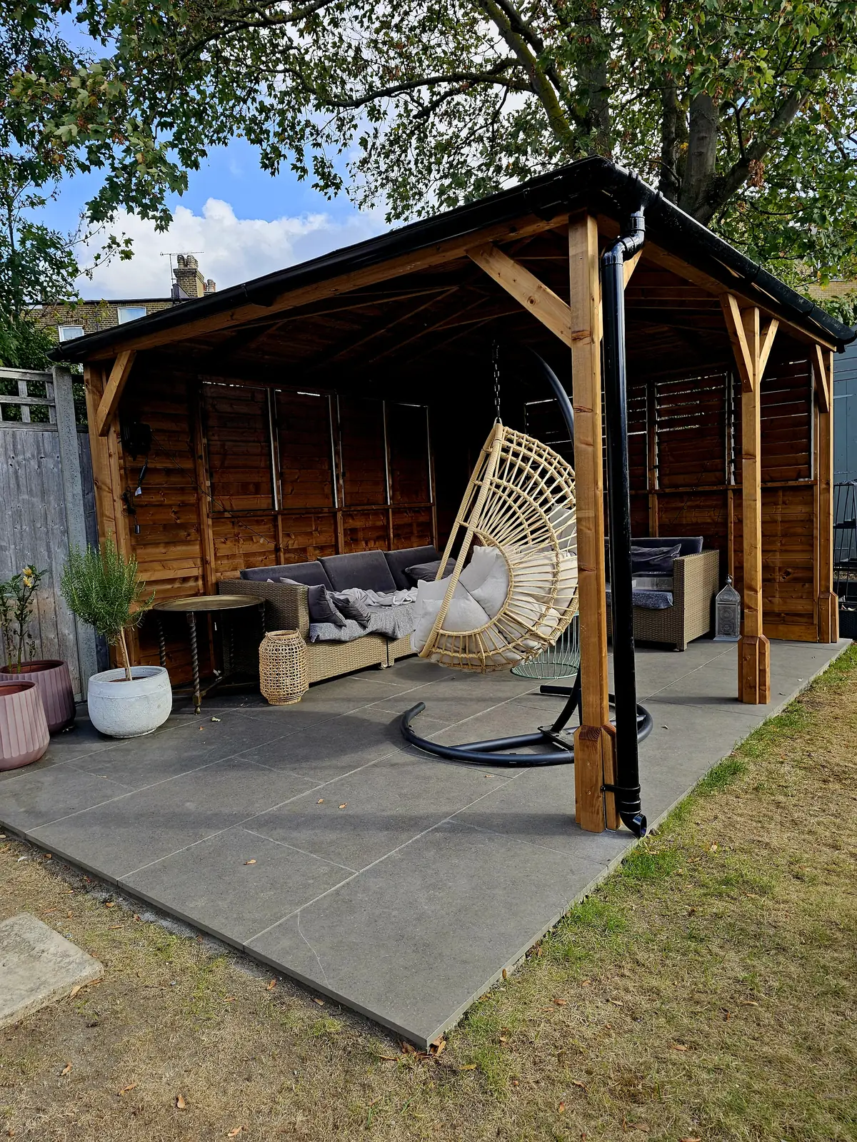 Timber gazebo with seating and a hanging egg chair on a grey porcelain patio in a Leytonstone garden
