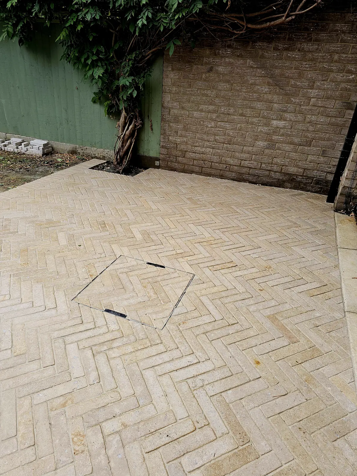 Herringbone Dijon limestone pavers meeting a brick wall and green fence in a Stratford garden