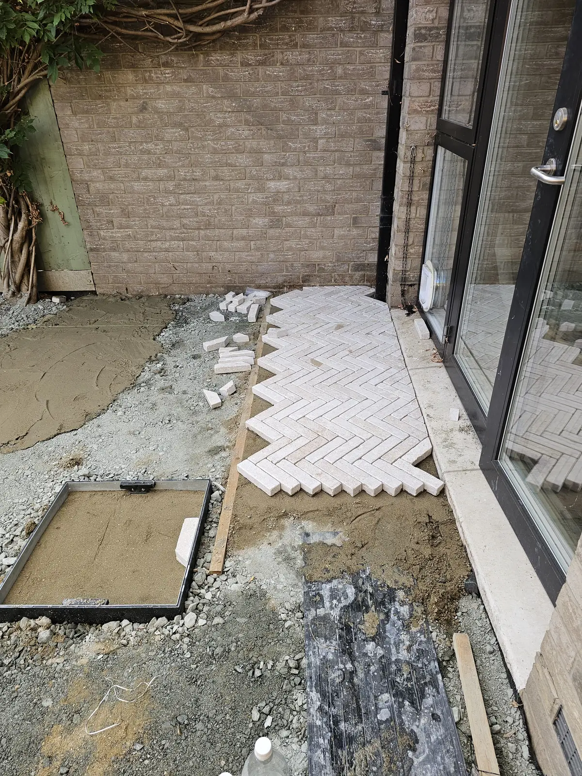 Herringbone pavers being laid outwards from the patio doors on the bedding layer